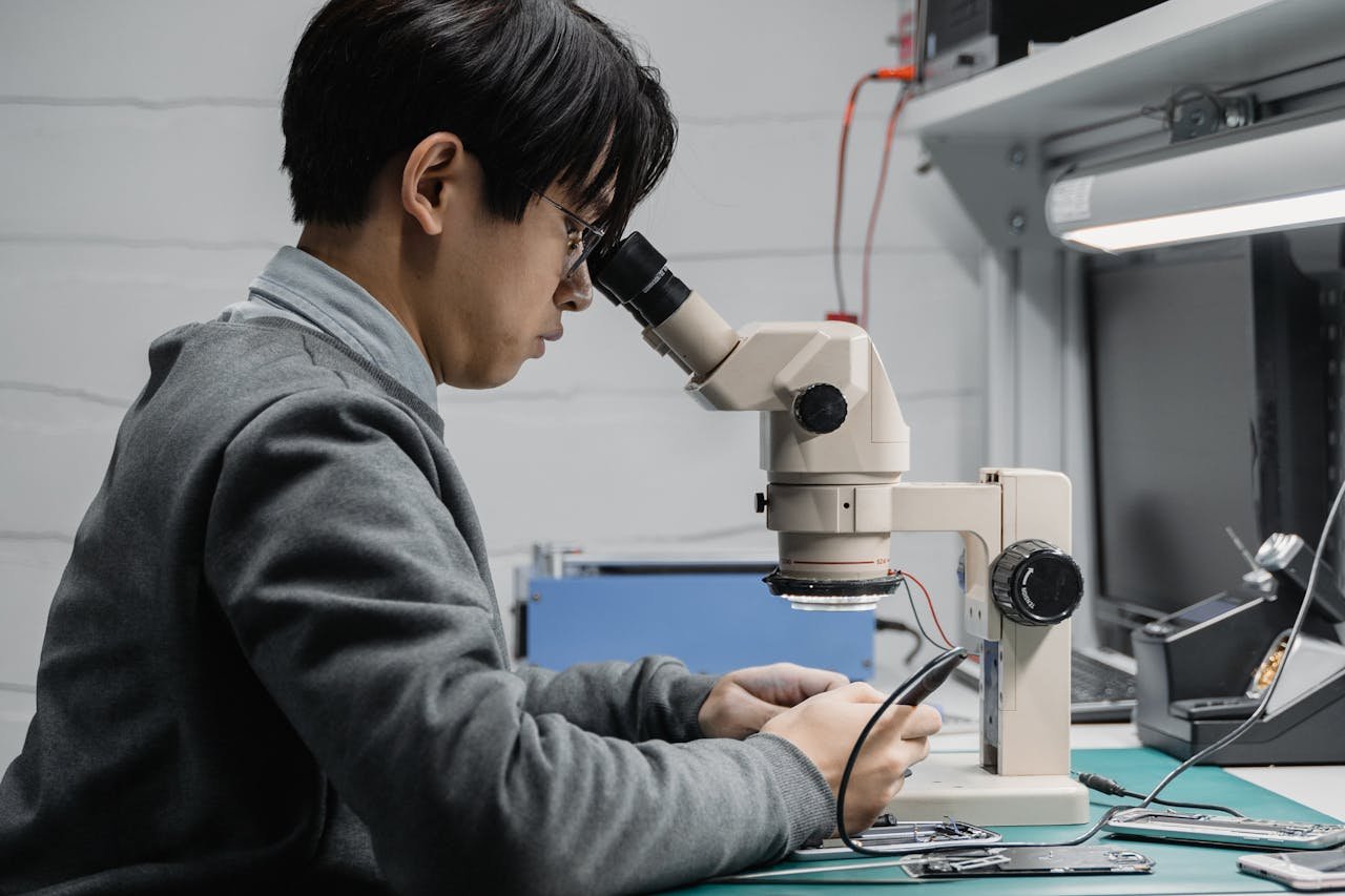 A focused technician repairing electronic components with a microscope in a lab.