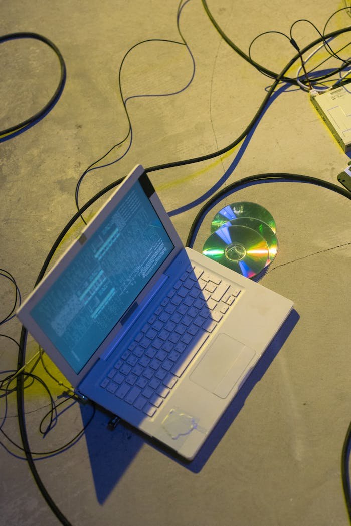 Top view of a laptop with cables and a CD on a concrete floor, highlighting technology and data concepts.