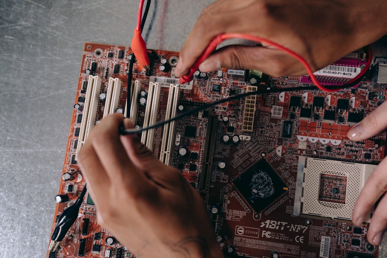 Close-up of hands working on a motherboard, showcasing electronic components and repair tools.